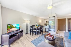 Ein modernes Wohnzimmer mit Flachbildfernseher, ein Essbereich mit Tisch und Stühlen, eine Küche mit Blick und ein Balkon.