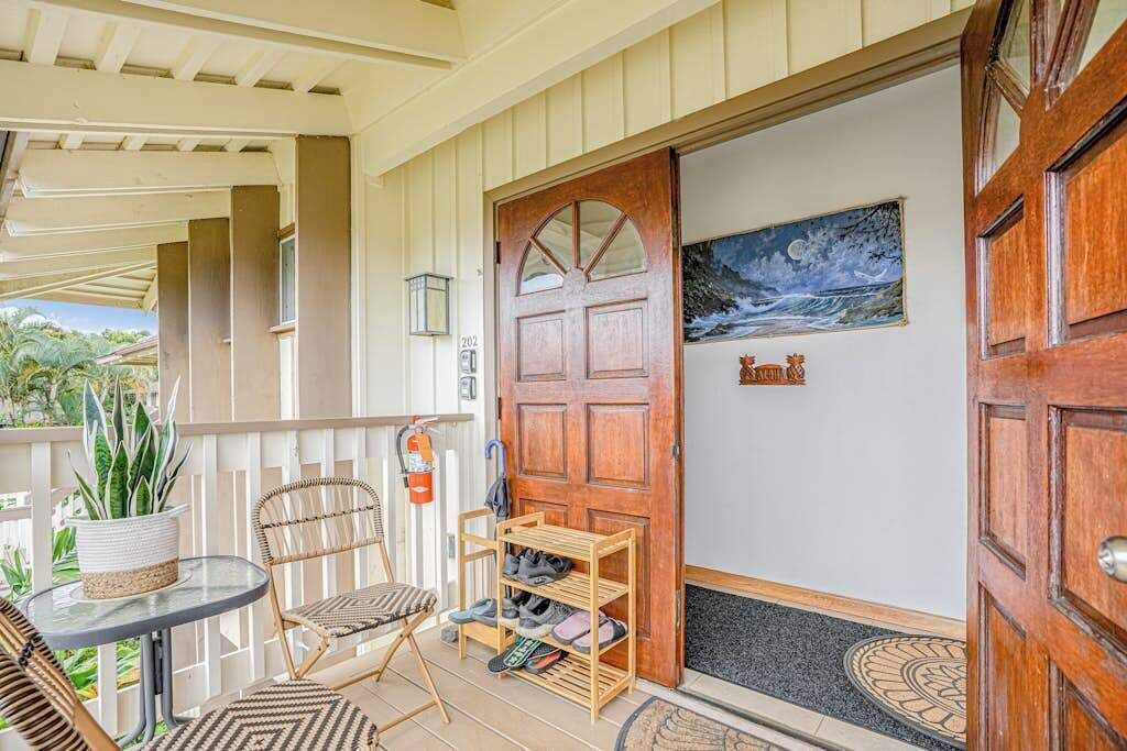 Un portico coperto con una porta in legno, un tavolino con sedie, un porta scarpe e una pianta in vaso.