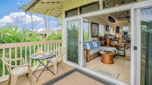 A covered balcony with a dining table and chairs, a sofa, and a wicker basket. - Princeville Paniolo 202A/202B Duplex- AC, Pool, Laundry- Hanalei Mountain Views (Princeville)