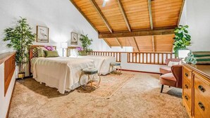 Un dormitorio con techo inclinado, una cama, dos sillas, un escritorio y un aparador.