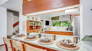 Een moderne keuken met een eethoek, houten kasten, een ingebouwde televisie en een raam met uitzicht op groen.