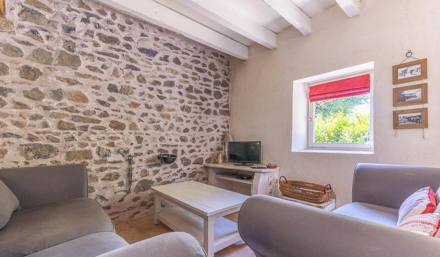 A room with stone walls, a television, a window with a red blind, and a wall-mounted picture frame.