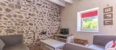 A room with stone walls, a television, a window with a red blind, and a wall-mounted picture frame.