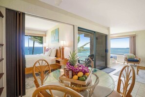 A hotel room with a bed, a dining table with fruit and flowers, a chair, a sofa, and a view of the ocean. - Oceanfront Sealodge Condo at Princeville w/ Kitchen, Essentials, Beach, Shopping (Princeville)
