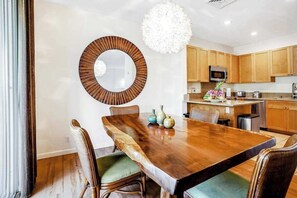 A modern kitchen with wooden cabinets, a central island, and a dining area with a large wooden table and wicker chairs. - *New* Two-Story Princeville Family Escape with Pool and AC (Princeville)