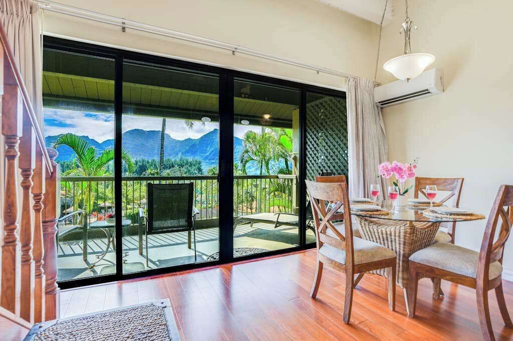 A room with a large sliding glass door leading to a balcony with a view of mountains and greenery.