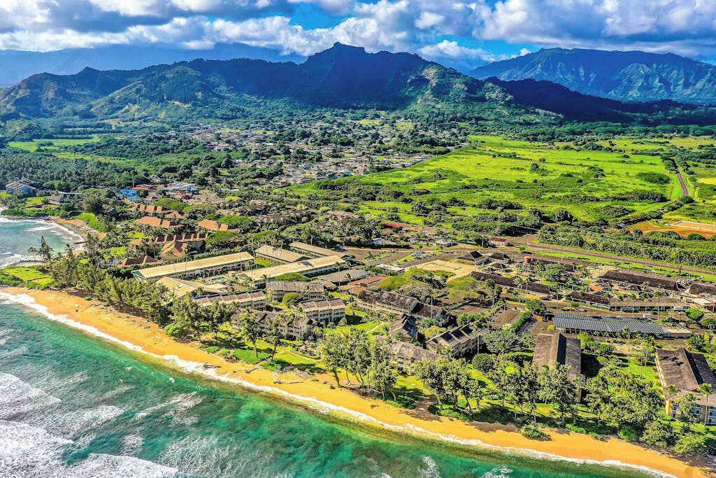 An aerial view of a coastal resort with multiple buildings, a beach, and surrounding greenery.