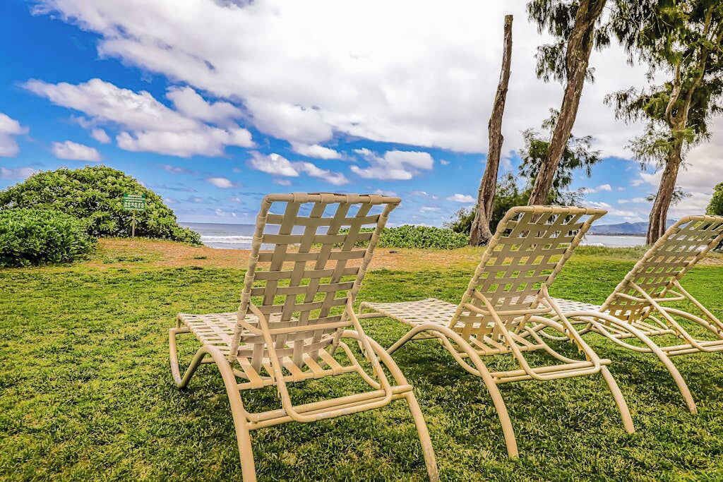 Deux fauteuils de jardin en osier, placés sur une pelouse verdoyante, offrent une vue sur l’océan et sur les arbres qui se dressent à l’arrière-plan.