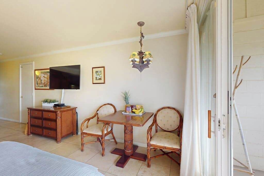 A dining area with a wooden table, two chairs, a television, and a ceiling fan.