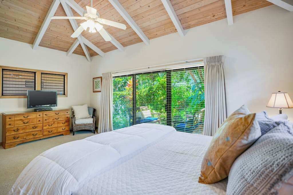 Un dormitorio con cama, cómoda de madera, televisor y ventana con persianas.