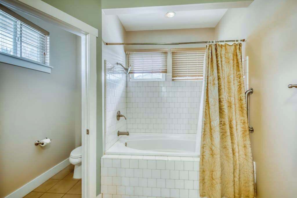 A bathroom with a bathtub, toilet, and window blinds.