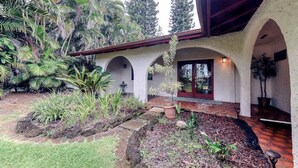 Un edificio con un porche cubierto, paseos con arcos y un jardín con plantas tropicales.