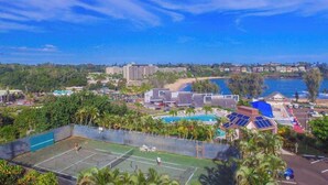 Ein Tennisplatz, umgeben von Gebäuden, einem Pool und einem Strand.