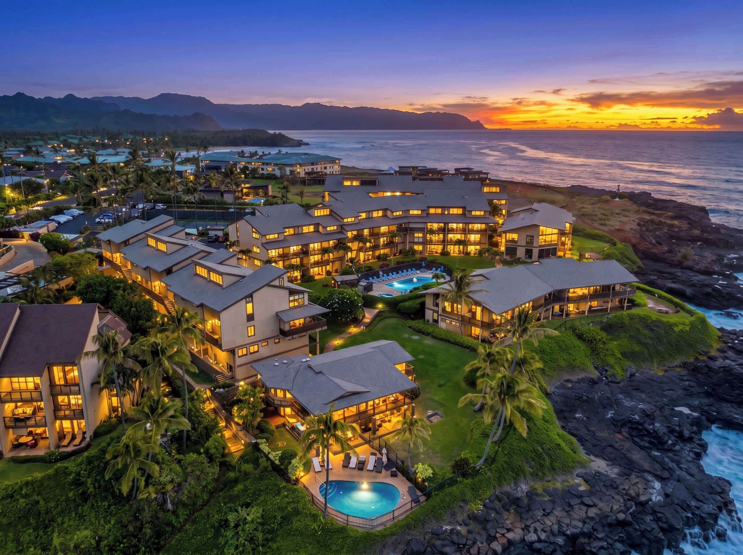 Un resort con varias edificaciones, una piscina y vista al océano al atardecer.
