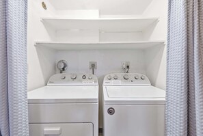 A laundry room with two Whirlpool washers and dryers, a white shelf above, and a power outlet on the wall. - Making Makahuena Memories in 2204 Villa- Pool/Ocean Views, Hot Tub, Kitchen+WIFI (Koloa)