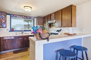 A kitchen with wooden cabinets, a window, a sink, and a countertop with a decorative bowl and bar stools. - Making Makahuena Memories in 2204 Villa- Pool/Ocean Views, Hot Tub, Kitchen+WIFI (Koloa)