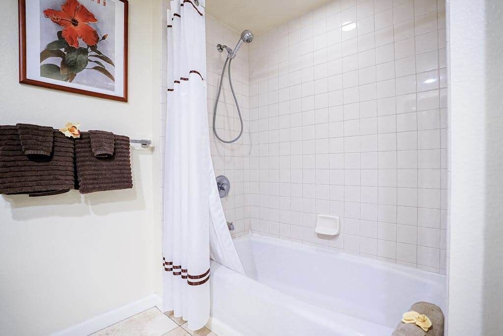 Een badkamer met een badkuip, een douche, witte betegelde wanden en een fotoraam met een bloem.