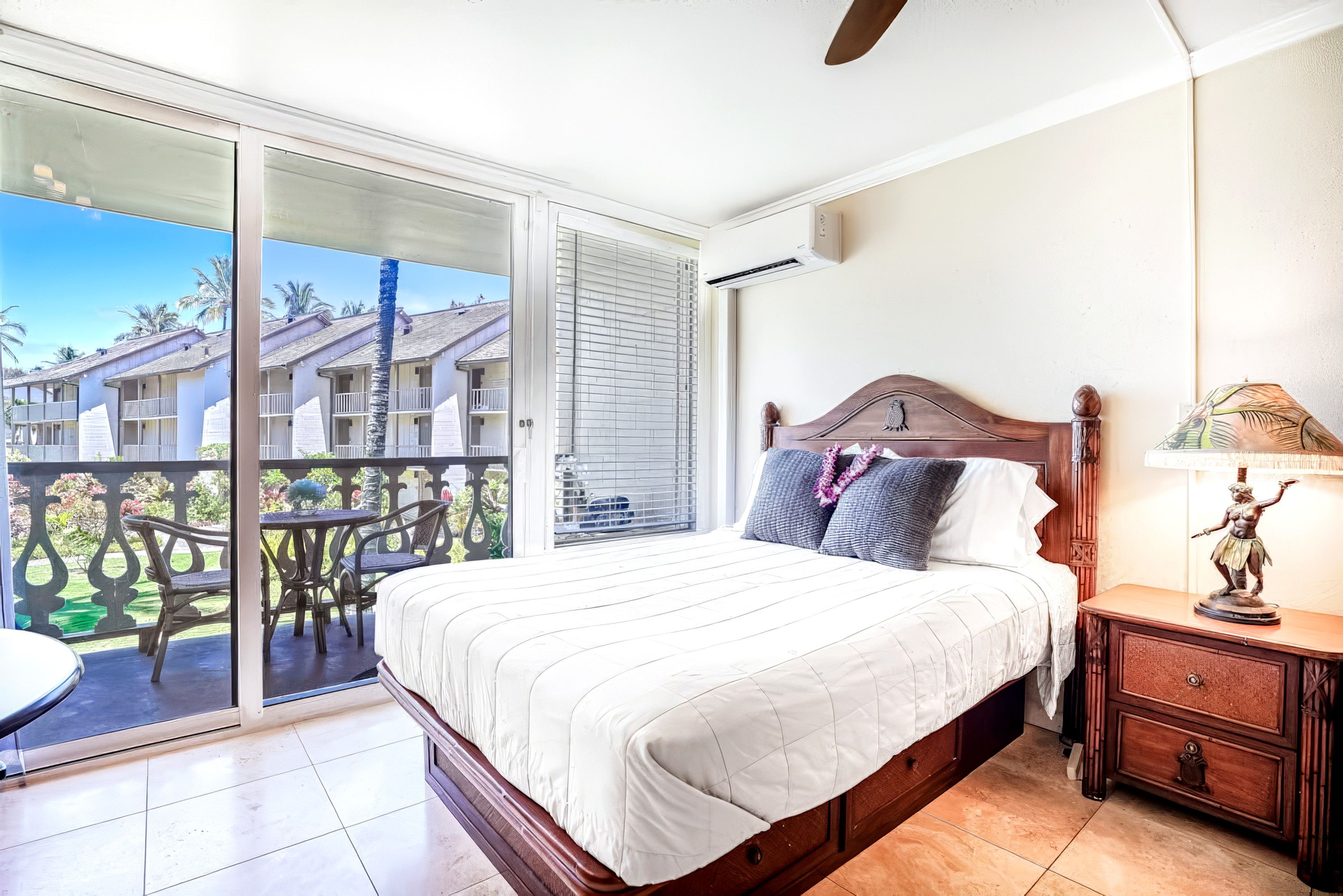 A hotel room with a bed, a nightstand, a lamp, and a view of a building through a sliding glass door.