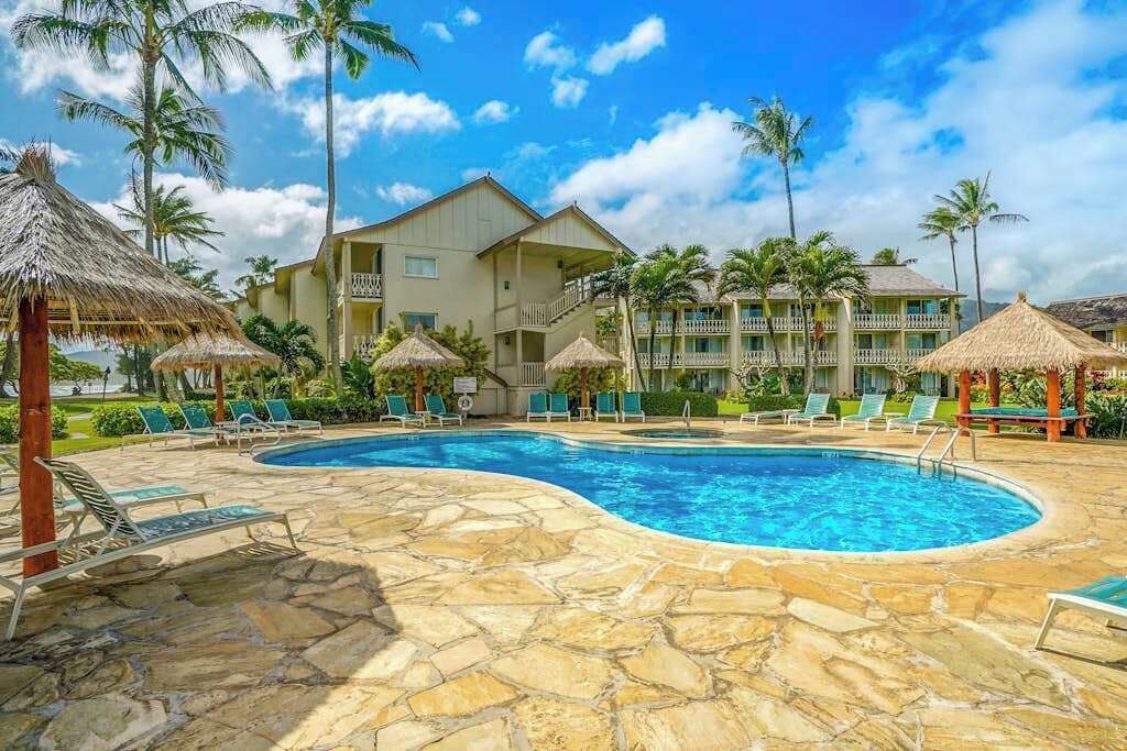 A swimming pool with lounge chairs, palm trees, and a hotel building.