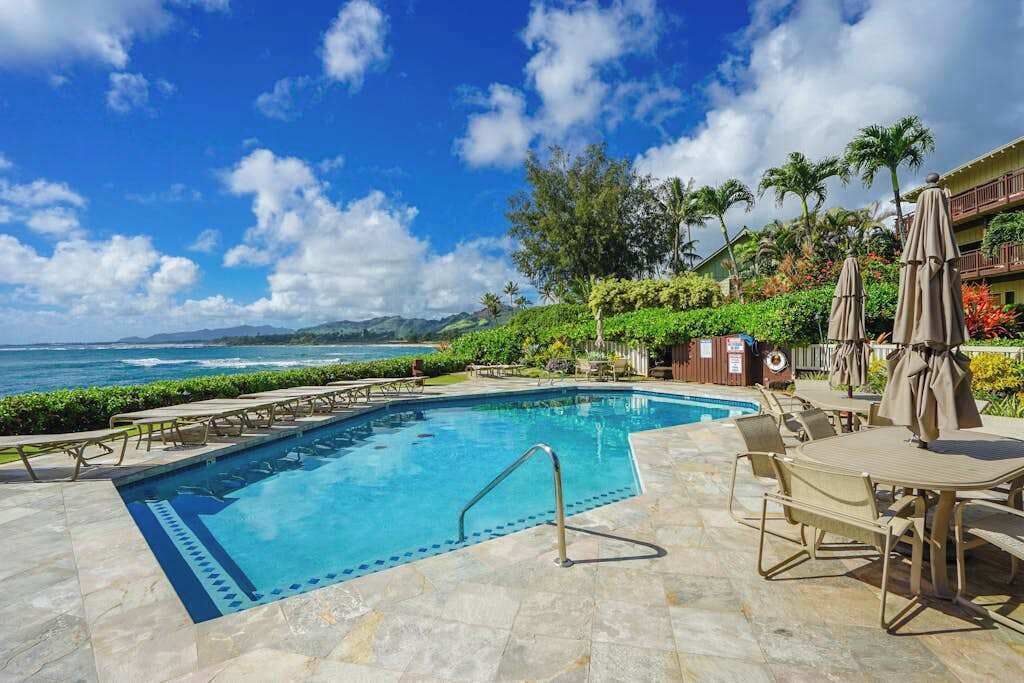 A swimming pool with a view of the ocean, surrounded by lounge chairs and umbrellas.