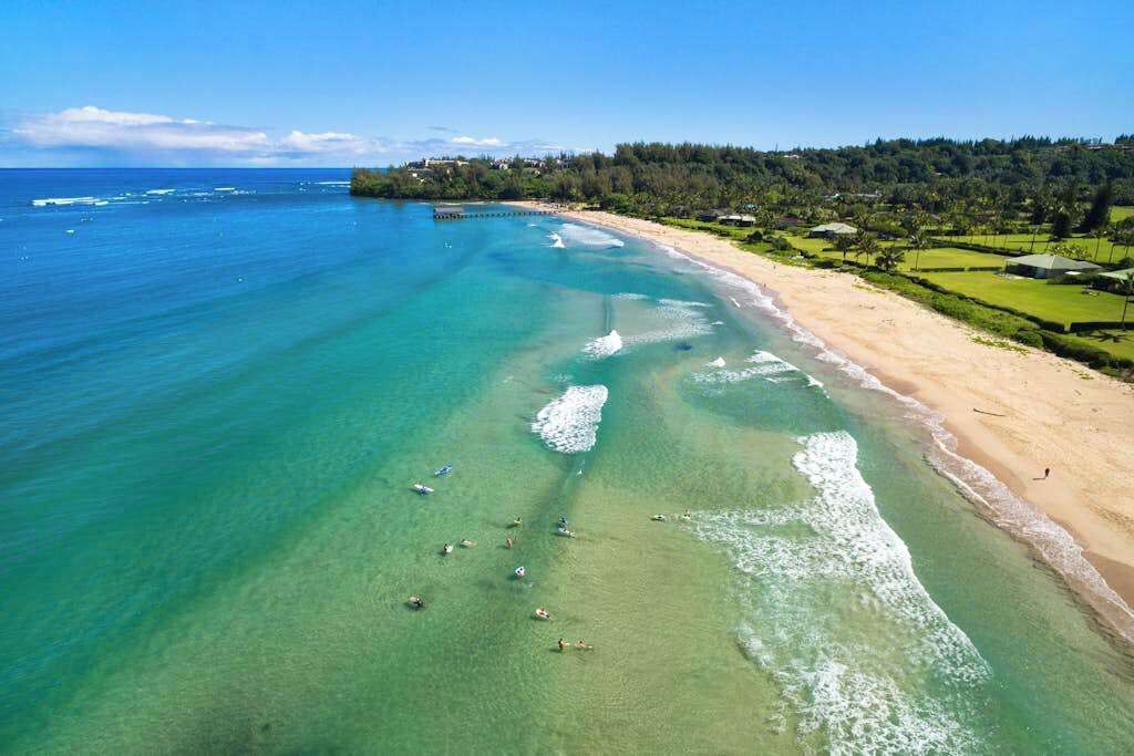 A beach with clear turquoise water, a sandy shore, and a forested hill in the background.