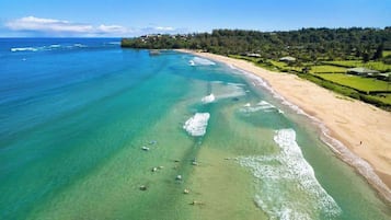 A beach with clear turquoise water, a sandy shore, and a forested hill in the background.