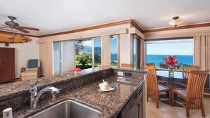 A kitchen with granite countertops, a sink, and a dining area with wooden chairs. - New Bali Hai and Hanalei Bay Views from Princeville Bluff (Princeville)