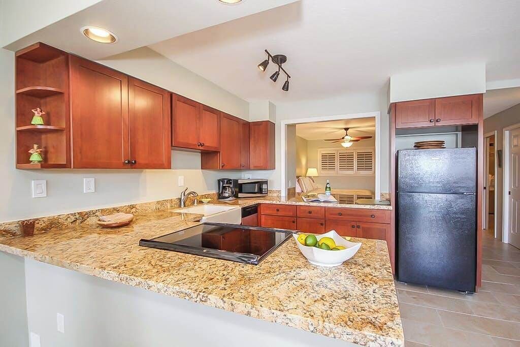 A kitchen with granite countertops, wooden cabinets, a black refrigerator, and a microwave.