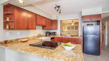 A kitchen with granite countertops, wooden cabinets, a black refrigerator, and a microwave.