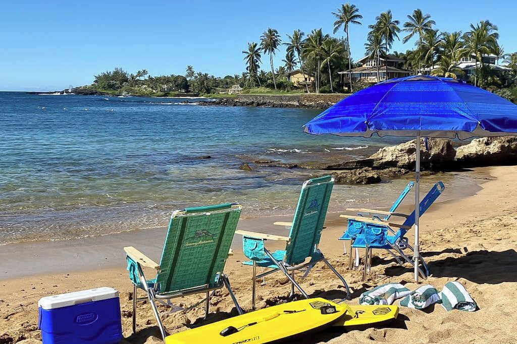 Une plage avec des chaises, une glacière et une planche de surf.