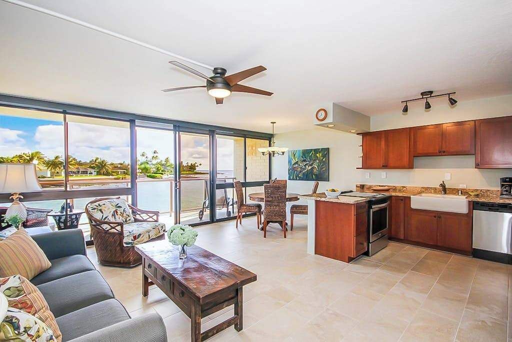 A modern kitchen with a dining area, large windows, and a ceiling fan.