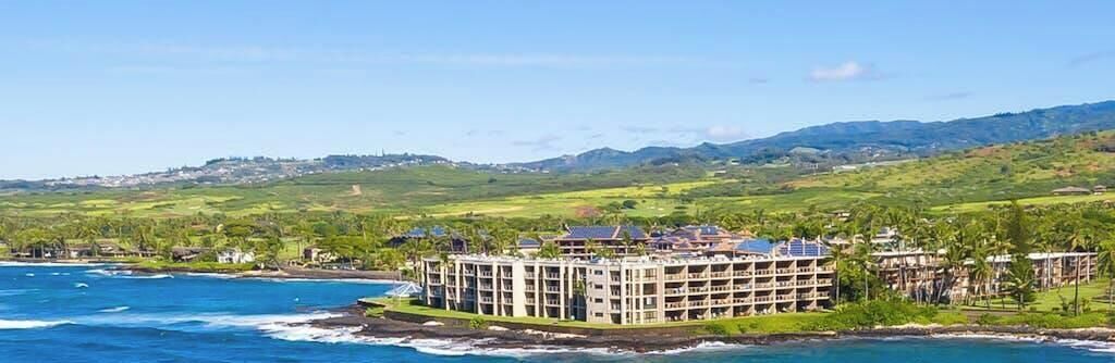 Un hotel frente al mar, con varios pisos y vistas al océano y las colinas.
