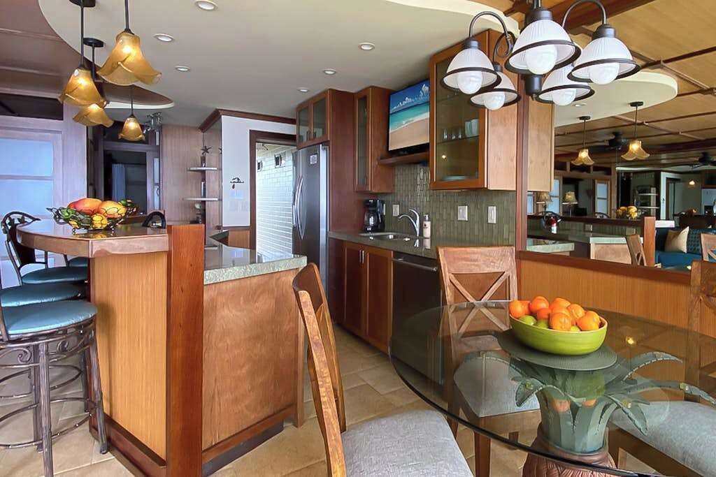 Une cuisine moderne avec des meubles en bois, un îlot central en verre et des luminaires suspendus.