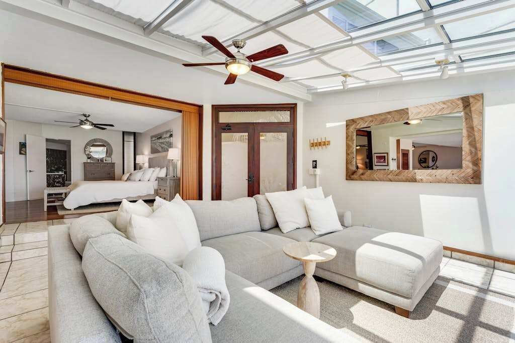 Een moderne woonkamer met een hoekbank, een plafondventilator en een grote spiegel.