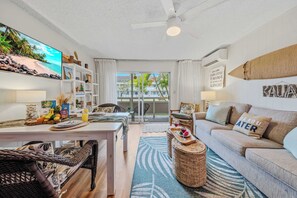 A well-lit living room with a sofa, a dining table, and a view of the outdoors through a glass door. - NEW Fall Sale Kapaa King Condo, 2-Minute Walk to the Ocean (Kapaa)