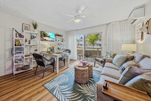 A modern living room with a dining area, a ceiling fan, and a view of the outdoors. - NEW Fall Sale Kapaa King Condo, 2-Minute Walk to the Ocean (Kapaa)