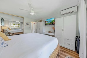 Un dormitorio con cama, ventilador de techo, televisor y armario.
