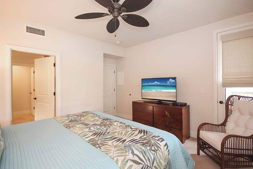 A bedroom with a bed, a ceiling fan, a television on a dresser, and a chair.