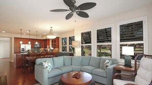 Un soggiorno con un divano componibile, un tavolino rotondo, una ventola a soffitto e vista panoramica attraverso ampie finestre.