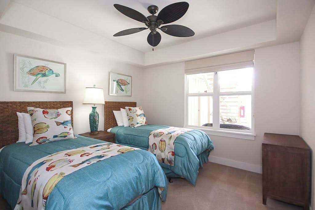 Une chambre avec deux lits, un ventilateur de plafond, des œuvres d’art accrochées aux murs et une fenêtre.