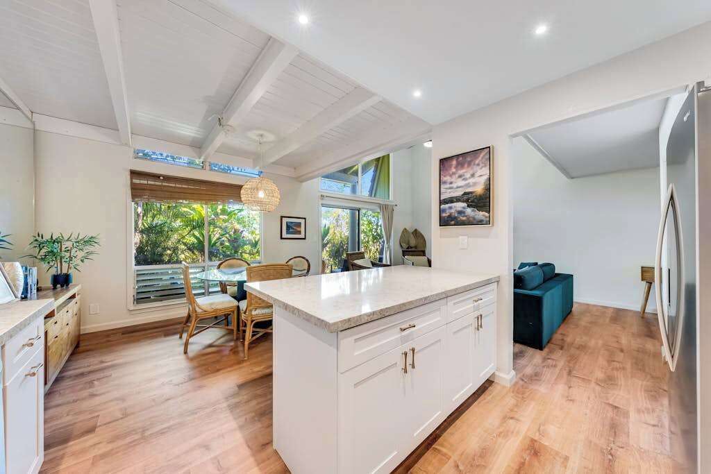 A modern kitchen with a central island, wooden flooring, and a dining area with natural light.