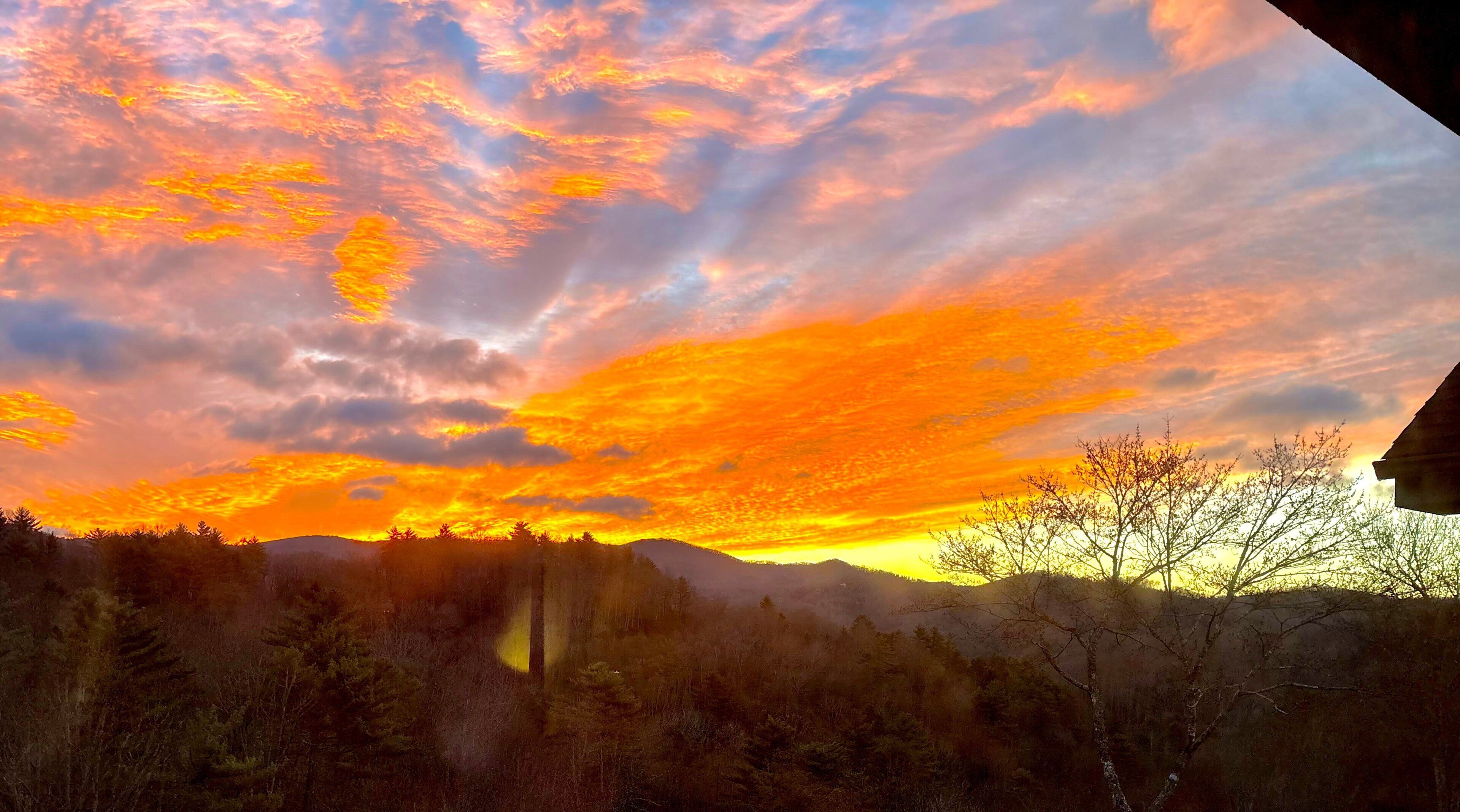 A sunset over a forested landscape with a house in the foreground.