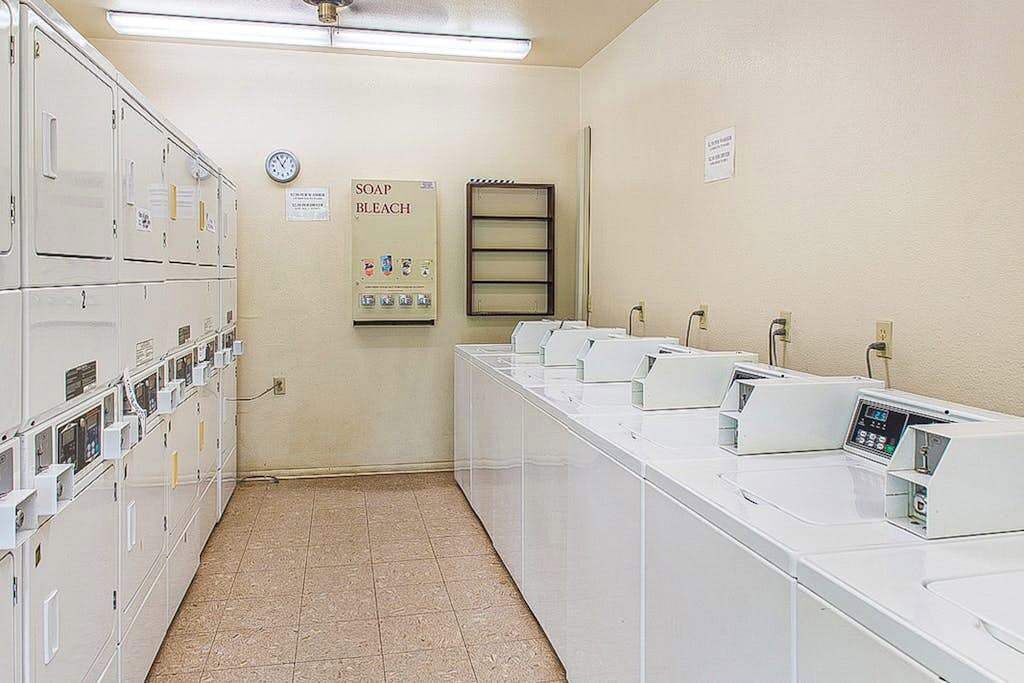 A laundry facility with multiple washing machines, a soap and bleach dispenser, and a clock on the wall.