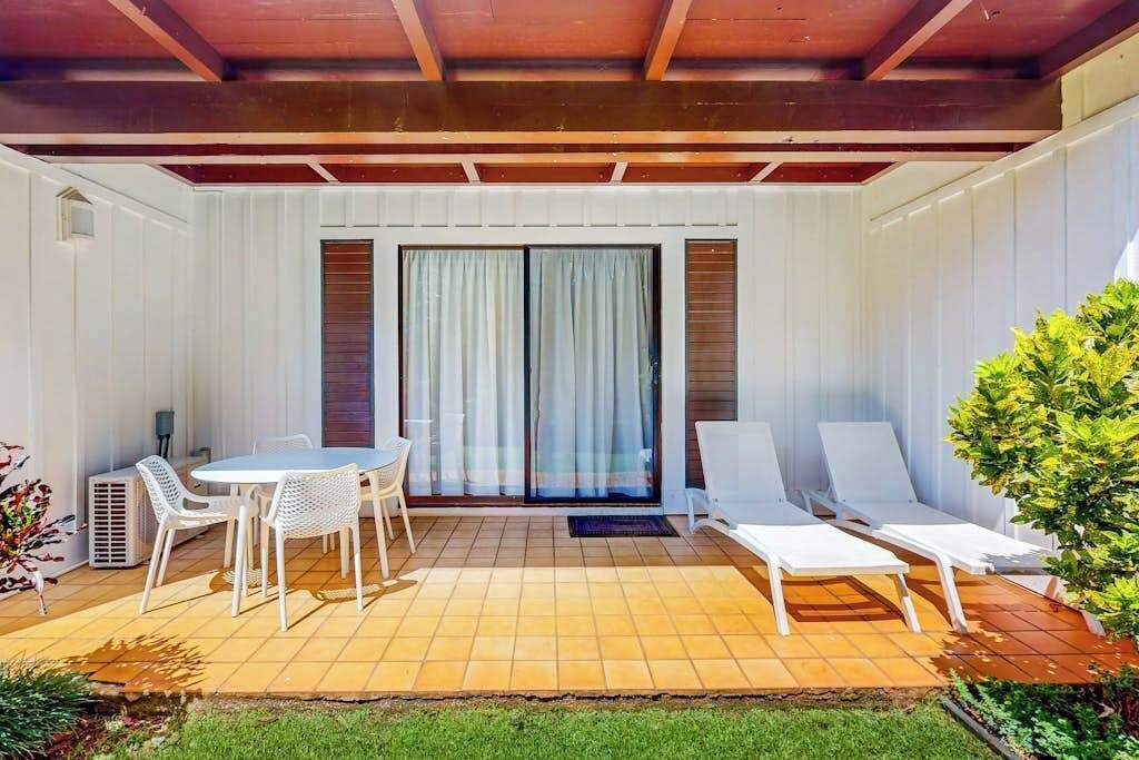 A covered patio with a table and chairs, a sliding glass door, and a small garden area.