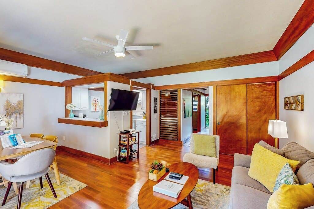 Uma sala de estar com televisão, vigas de madeira, ventilador de teto e sofá.