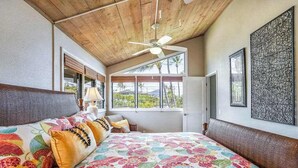 A bedroom with a large bed, a ceiling fan, a window with a view, and a door. - New Fall Sale Breezy Two-Story Poipu Escape with Pool and Hot Tub (Koloa)