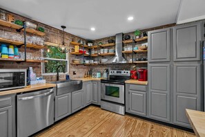 A modern kitchen with grey cabinets, stainless steel appliances, wooden countertops, and a brick wall. - Beech on The Rocks | pet friendly, club access, mtn views (Banner Elk)