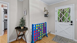 En hall med en dörr, ett litet bord med en växt, ett färgglatt brädspel och en matta vid ingången.