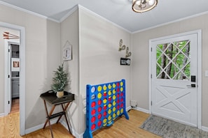 A hallway with a door, a small table with a plant, a colorful board game, and a mat at the entrance. - Beech on The Rocks | pet friendly, club access, mtn views (Banner Elk)