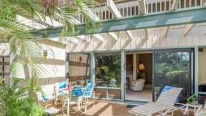 Een overdekt buitengebied met een zwembad, lounge stoelen en een glazen schuifdeur naar een woonkamer.
